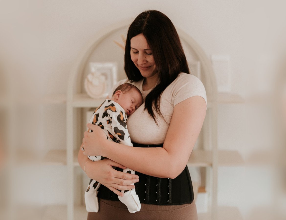 A smiling mother wearing the MumWrap holds her sleeping newborn