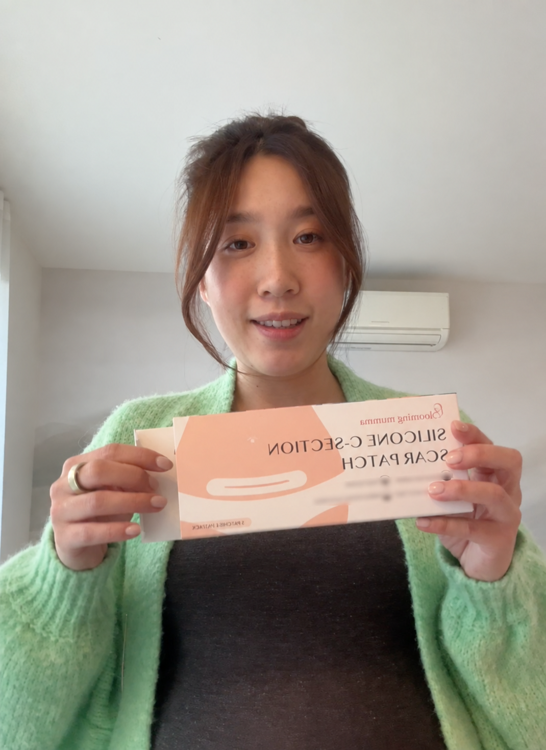 Customer holding Blooming Mumma Silicone C-section Scar Patch packaging, with small benefit claims blurred.